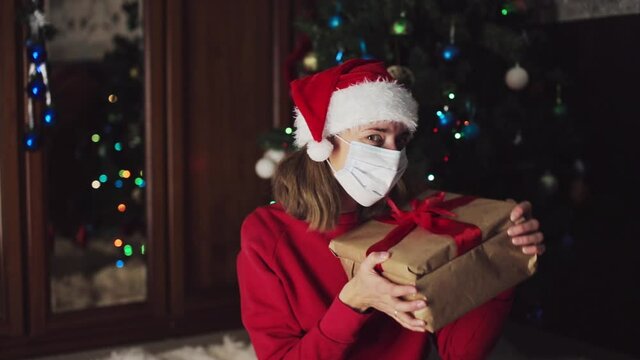 girl in red clothes and medical mask unfold New year gifts. the concept of celebrating Christmas midnight. Holiday's decor boce, Christmas tree