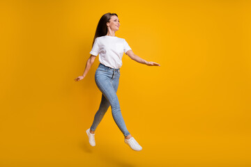 Fototapeta na wymiar Full length body size photo of girl jumping up walking looking at empty space isolated on bright yellow color background
