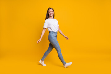 Full length body size photo of girl stepping forward looking at copyspace smiling isolated on bright yellow color background