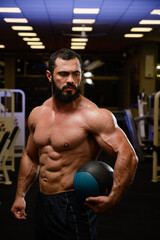 Fototapeta na wymiar strong bearded man with medicine ball in fitness sport gym at night
