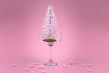 Christmas tree with pink decoration in glass of champagne on pink background. Christmas composition. New year minimalistic composition. Holiday concept.