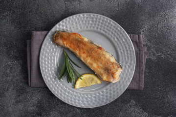 Fried fish hake Pollock and slices of fresh lemon. Dark concrete background. Copy space.