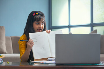 Young girl showing the spellings of the words her teacher dictated in front of the laptop during...
