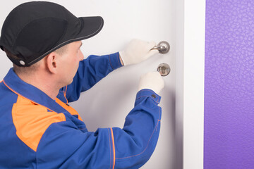 a man, a locksmith, repairs the lock of the front door, close-up