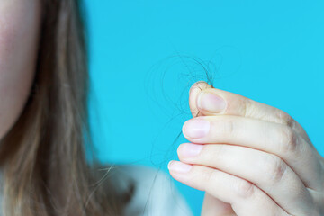 Girl holds strand of hair front view on blue background, hair loss concept