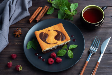 A piece of double-layer cake on a plate of chocolate brownies and curd cheesecake with raspberries. Dark background copy space