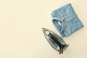 Iron and folded jeans shirt on white background, top view
