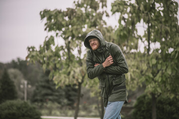 Young bearded man in a hood going under the rain