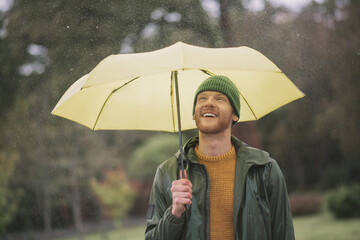 Young bearded man standing with yellow umbrella in hand