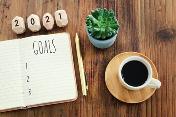 Business concept of top view 2021 goals list with notebook, cup of coffee over wooden desk
