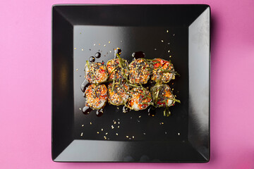 Sushi set served on a black square plate over bright pink background. Traditional Japanese cuisine, sushi rolls close up