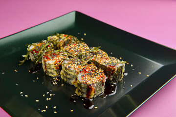 Sushi set served on a black square plate over bright pink background. Traditional Japanese cuisine, sushi rolls close up