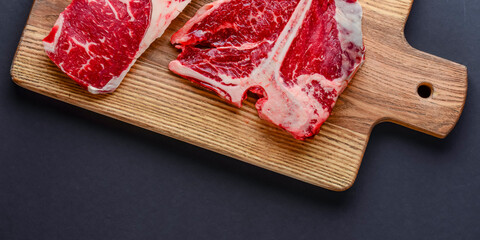 Fresh raw beef steak on wooden cutting board, top view. Served over black background.