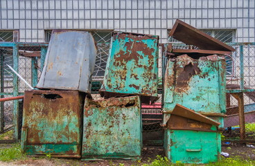 Old empty green dirty and rusty garbage containers in the backyard of an old building