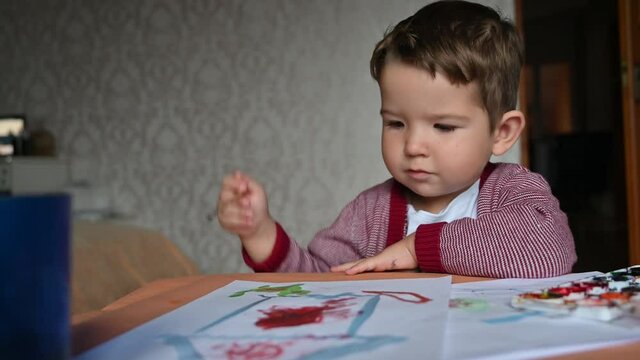 Child using brush and painting something on the paper. Portrait of cute drawing brunet child. 