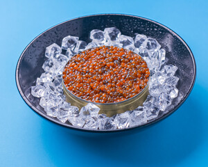 Bowl of red caviar on vintage black metal tray with ice over bright blue background. Top view, copy space, flat lay.