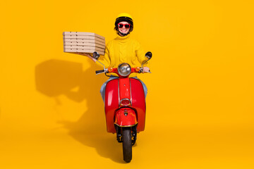 Photo portrait of smiling woman delivering pizza driving red retro scooter isolated on vivid yellow...