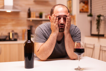 Man being sad and hangover after a bottle of red wine in home. Unhappy person disease and anxiety feeling exhausted with having alcoholism problems.