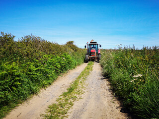 A tractor in a country lane with high hedges around the edge of a field. Rural farming concept during harvest season - UK