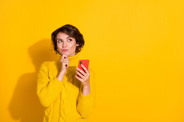 Photo portrait of curious dreamy girl holding smartphone looking at blank space isolated on vivid yellow color background