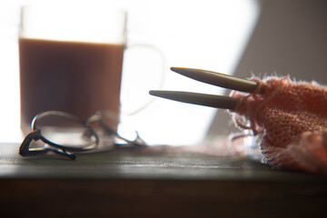 Close up of a knitting needle in a half knit muffler kept on a table with   a glass of tea and...