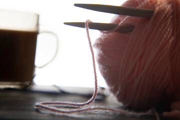 Close up of knitting needles kept in a yarn ball with tea kept in the background	