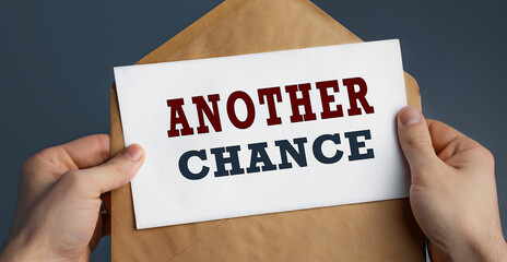 Closeup of a Male hands holding craft envelope with text ANOTHER CHANCE on blue background