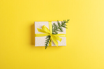 Christmas DIY gift box decorated with yellow ribbon with bow and green twig of arborvitae in center.