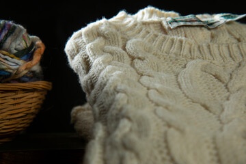 White knitted sweater kept on the table next to a basket with colorful yarn balls in it	