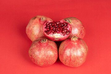 4 large red pomegranate and one half cut pomegranate on red background