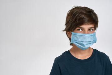 Portrait of little sportive boy child in sportswear wearing medical mask, looking aside, standing isolated over white background