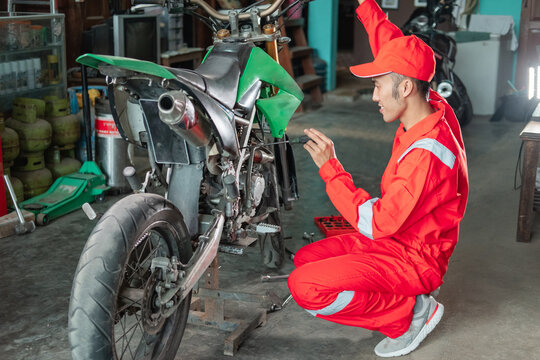 male mechanic squats down the carburetor using the screwdriver next to the motorbike in the garage