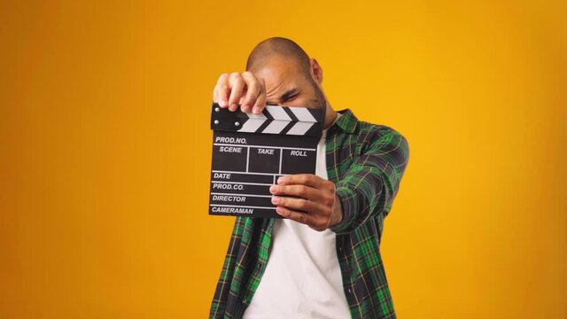Casual young african american man claps clapperboard against yellow background