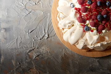 food, culinary, baking and cooking concept - close up of pavlova meringue cake decorated with berries on wooden serving board