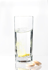 A large, white tablet with dissolves in a glass of water on a white background. Vitamin C.
