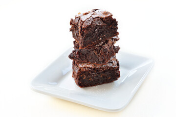 A small tower of chocolate brownies served on a square plate.