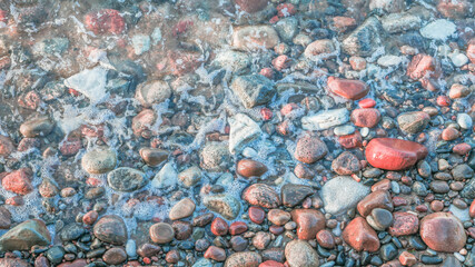 sea foam on wet pebbles on the beach on a sunny day, close up