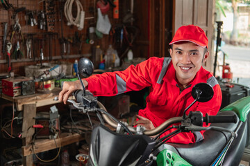 smiling mechanic in wearpack uniform checking dirt bike engines throttle in garage