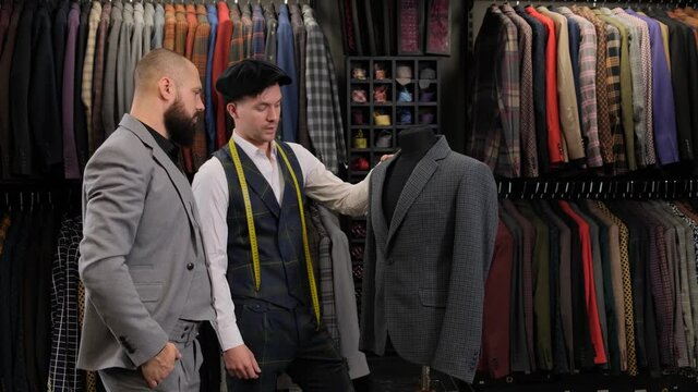 Slow motion of handsome man choosing a suit design with tailor in atelier. designer presenting the costume on the menequin to the buyer at the clothing store