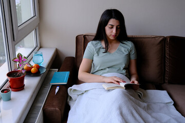 Woman patient lying on the sofa trying to spend time reading a book.