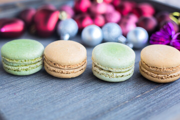 Four fresh pistachio and caramel macaron on grey wooden surface. Christmas balls and decorations in background. Green and beige round sweets closeup. Winter cafe menu. Traditional french dessert 