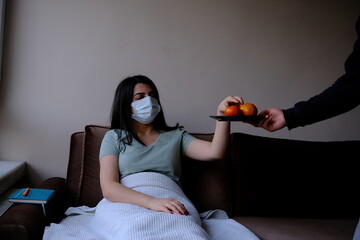 the corona patient lying on the sofa takes the fruits handed to him. Attention is paid to the use of personal protective equipment.
