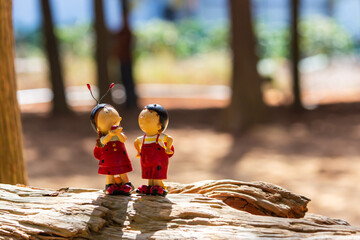 A doll in the shape of a ladybug stands on a wood in the woods, as if talking to a companion