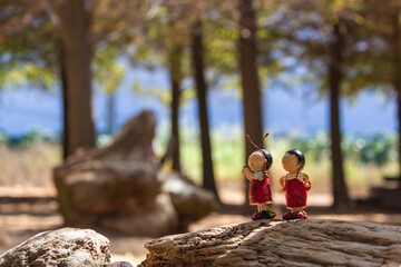 A doll in the shape of a ladybug stands on a wood in the woods, as if talking to a companion