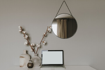 Blank screen laptop. Home office desk table workspace with cotton plant, vase, mirror on grey...