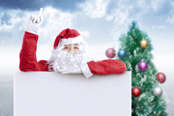 Asian man in Santa costume with the board and Christmas tree with a snowy background