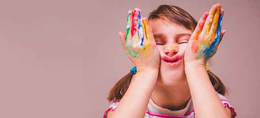 Funny portrait of happy beautiful young child girl makes faces with children's makeup and painting colorful hands. Free space for text or design.