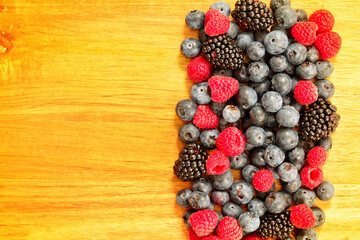 Background with fresh summer berries on a bamboo chopping board. Raspberries, blueberries, and blackberries groupped on the right side of the board.