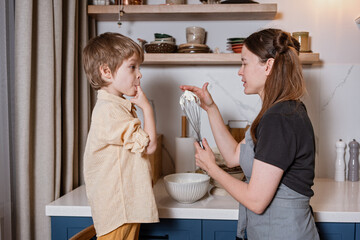 Cooking together concept. Mom and son having fun while decorating layered carrot cake in the kitchen in Scandinavian style