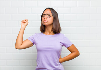 latin woman feeling serious, strong and rebellious, raising fist up, protesting or fighting for...